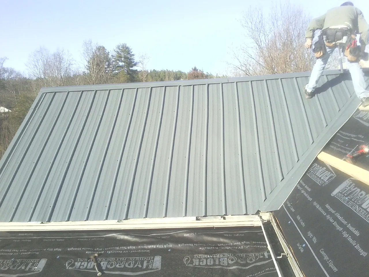 Crew installing dark green standing seam panels over synthetic underlayment in Clarksville